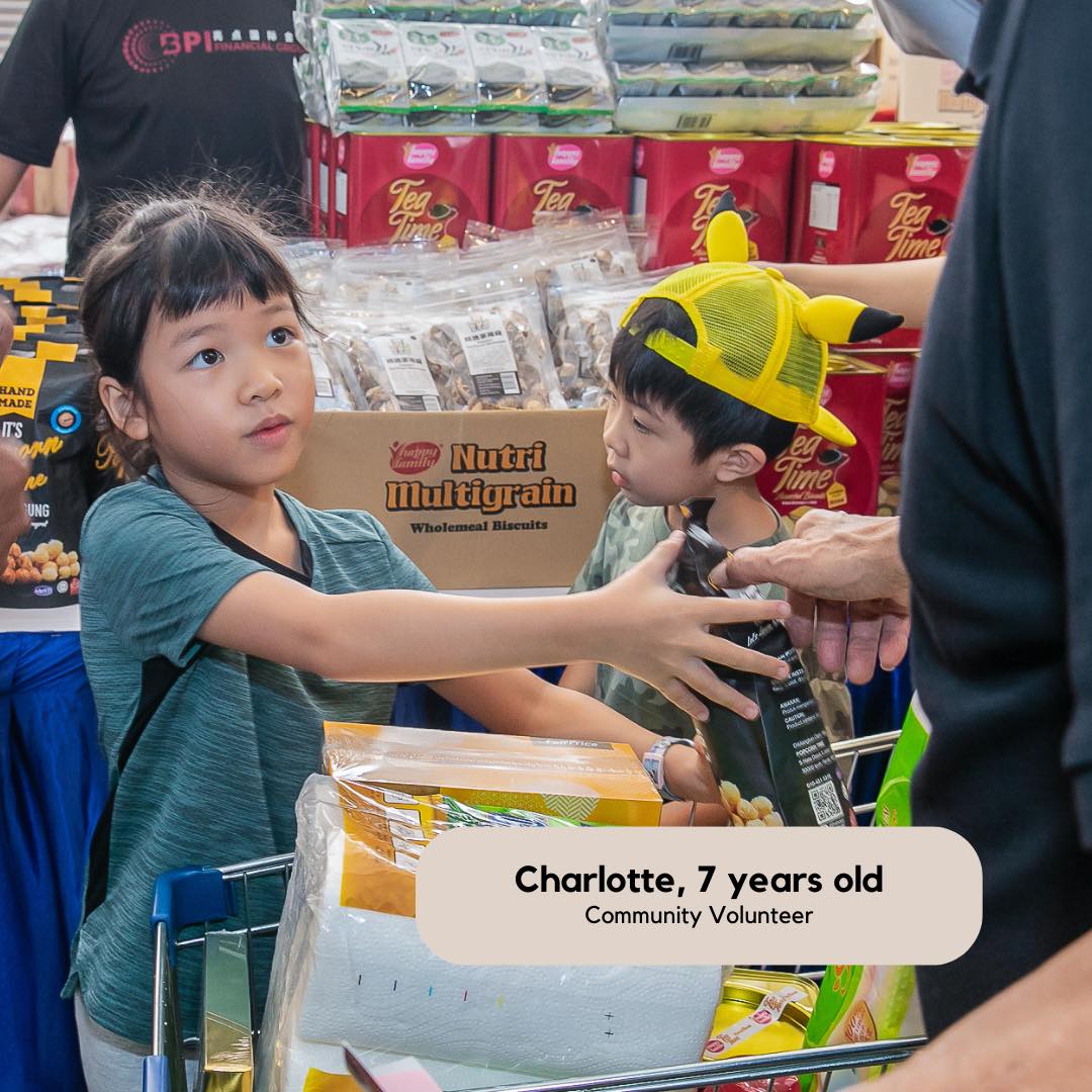 Young girl volunteer passes a packet of peanuts to an elderly man off-screen